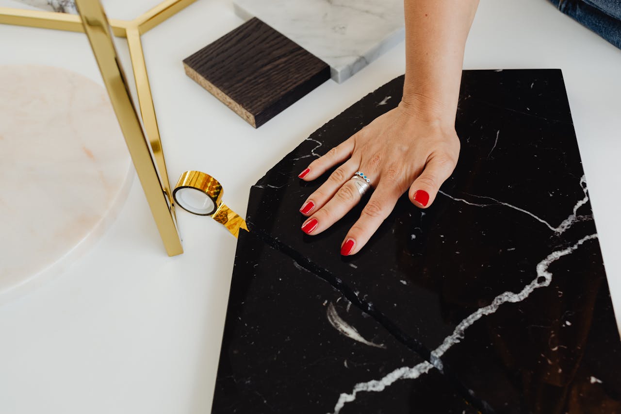 our-story Close-up of a hand with red nails touching black marble, showcasing elegance and modern design.